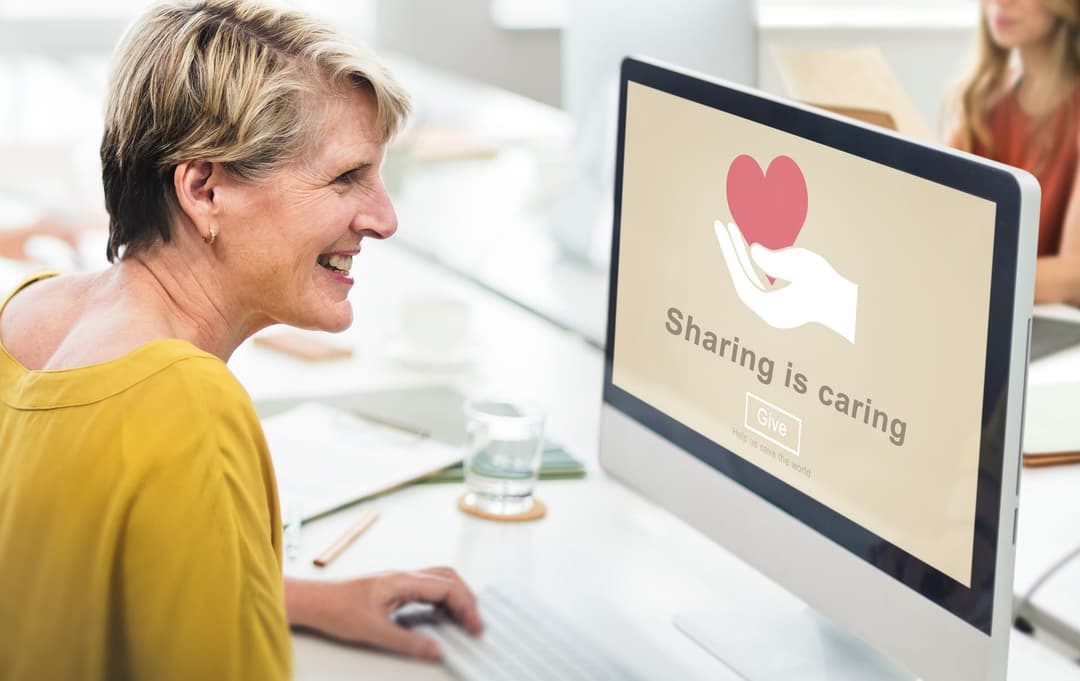 A smiling woman looking at a computer screen displaying a donation message with a heart icon